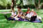 Sigrid and five children sit on picnic blanket as she reads a story, with two open suitcases beside them