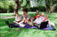 Sigrid and five children sit on picnic blanket as she reads a story, with two open suitcases beside them