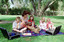 Sigrid and five children sit on picnic blanket as she reads a story, with two open suitcases beside them