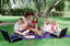 Sigrid and five children sit on picnic blanket as she reads a story, with two open suitcases beside them