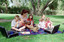 Sigrid and five children sit on picnic blanket as she reads a story, with two open suitcases beside them