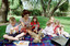 Sigrid and five children sit on picnic blanket as she reads a story, with two open suitcases beside them