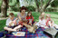 Sigrid and five children sit on picnic blanket as she reads a story, with two open suitcases beside them