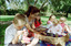 Sigrid and five children sit on picnic blanket as she reads a story, with two open suitcases beside them