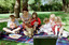 Sigrid and five children sit on picnic blanket as she reads a story, with two open suitcases beside them