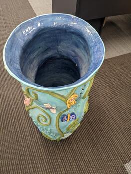 Light blue pot with vines, leaves, flowers, insects and words written in cursive and braille