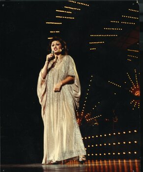Jennifer Murphy singing on stage wearing a long flowing silver sequined gown.