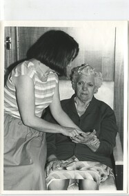 Younger woman fingerspells on to the palm of an older woman