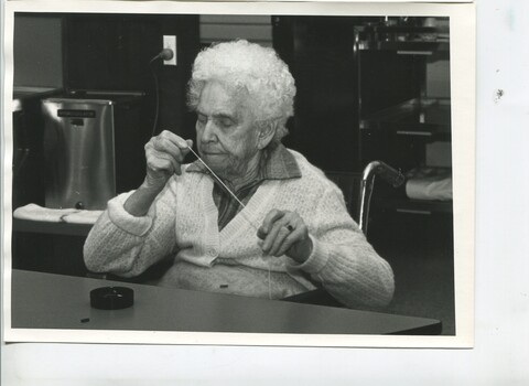 Elderly woman in wheelchair stretching string or thread between her fingers