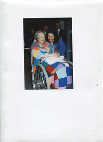 Younger woman in blue suit leans down towards older woman in wheelchair