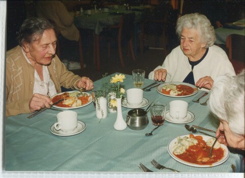 Three women sit at a table eating stewed meat and vegetables for lunch