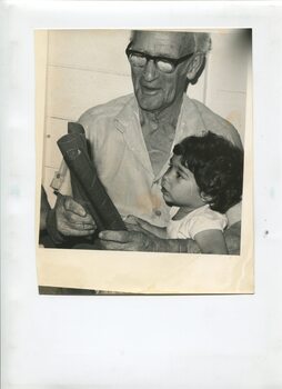 Older man holds young girl in his lap as he taps two paper cylinders together