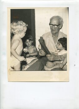 Older man holds young girl in his lap, with two other children looking on