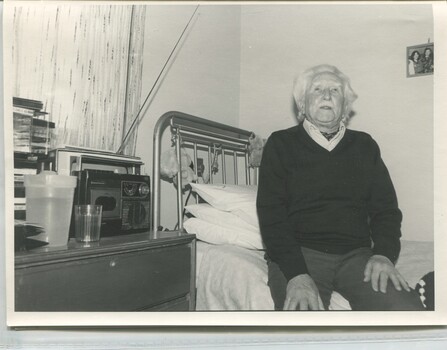 A man sits on the edge of his bed with his belongings around him