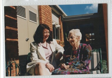 Staff member sits beside elderly female outside