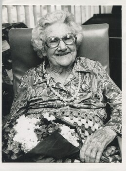 Centenarian woman sits in chair, holding a bunch of flowers