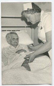 Elderly woman rests in bed under a sheepskin with a nursing sister