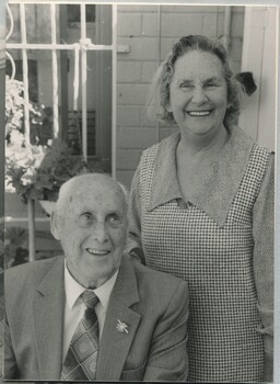 Man seated on chair wearing suit with AFB lapel pin and woman standing behind him