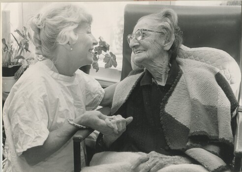 Elderly woman sits in a chair whilst a staff member kneels beside her
