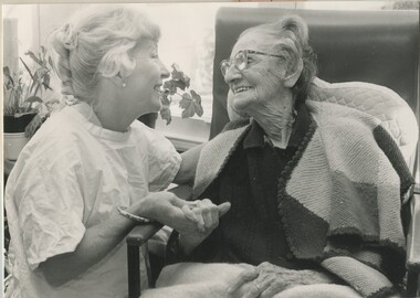 Elderly woman sits in a chair whilst a staff member kneels beside her