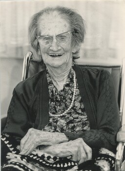 Elderly woman sits in wheelchair and smiles for camera