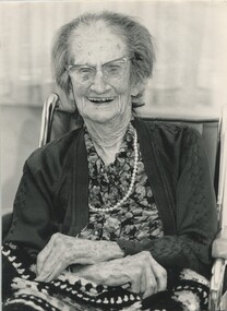 Elderly woman sits in wheelchair and smiles for camera