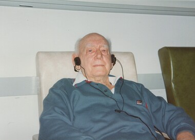 Seated man wearing headphones as he looks to camera