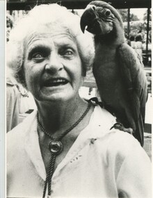Doris Nothing and macaw parrot on her left shoulder look to camera