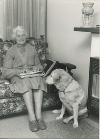 Older woman sits on lounge reading a Braille book and with a Labrador by her legs