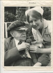Elderly man receives a carnation for his buttonhole from Nurse Poley