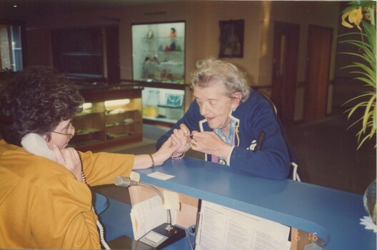 A receptionist assists a resident with her jewellery or watch