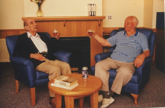Two male residents raise their beers in the lounge room