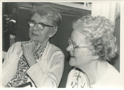 Two seated ladies - one laughs as the other looks on