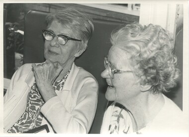 Two seated ladies - one laughs as the other looks on