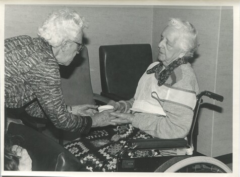 Woman handing a cup of tea to another in a wheelchair