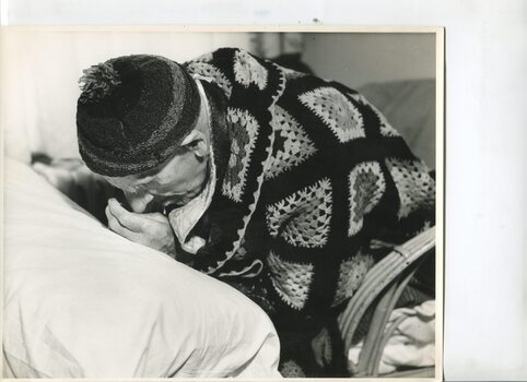Elderly man bent forward towards a pillow in front of him