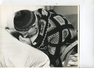 Elderly man bent forward towards a pillow in front of him