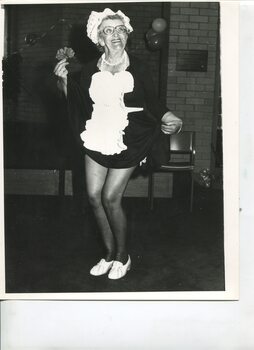 Older woman smiles as she raises the skirt of her maid costume