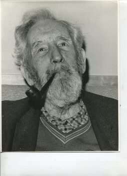Older man smokes a pipe as he faces camera