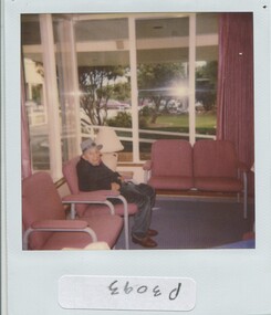 Older man sits in a lounge with a view over the front garden