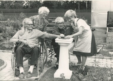 Three residents and one staff member observe and feel a sundial in the garden