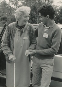 An older woman with cane is assisted from the car by a younger male