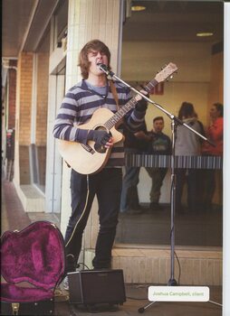 Joshua Campbell plays guitar, busking in a retail shopping strip