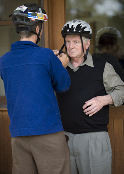 Older man being assisted with a bike helmet by a younger man