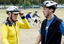 Man in yellow biking helmet speaking with another man in blue as tandem cycle passes in background