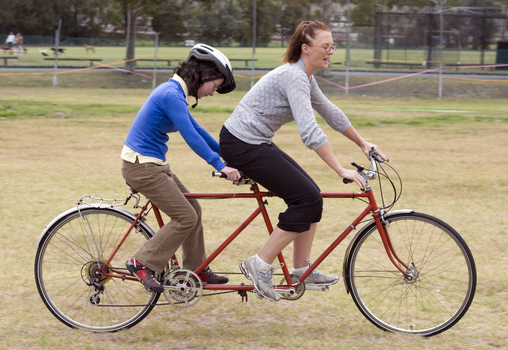 Two women on tandem cycle, one with helmet and the other without