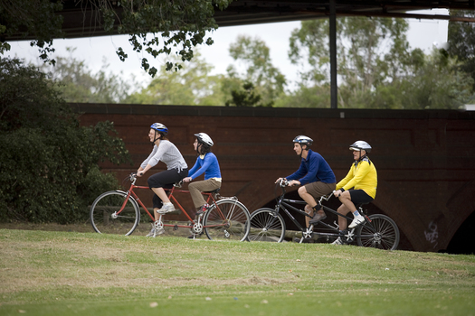 Two tandem cycles riding beside the creek and freeway overpass