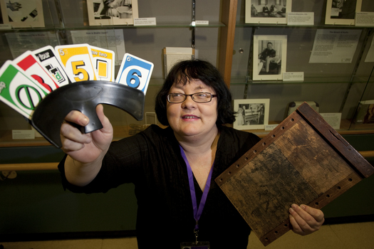 Michele Prentice holding a card holder with Braille UNO cards and a base board for a braille frame