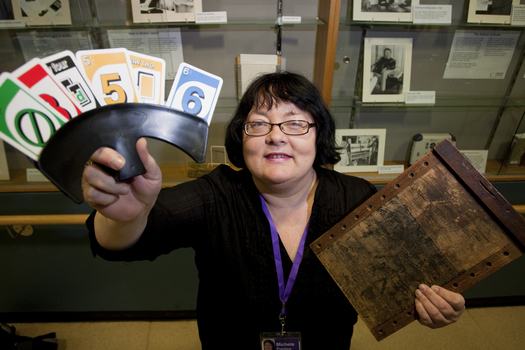 Michele Prentice holding a card holder with Braille UNO cards and a base board for a braille frame