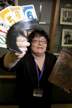 Michele Prentice holding a card holder with Braille UNO cards and a base board for a braille frame